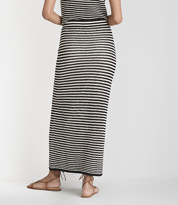 A person wearing a black and white striped maxi skirt and brown sandals stands against a plain white background.