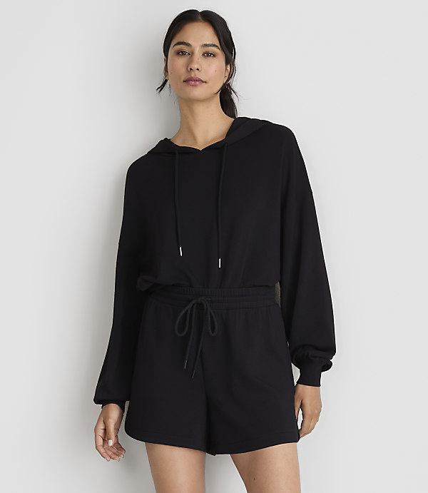 A woman in a black hoodie and shorts stands against a plain white background.