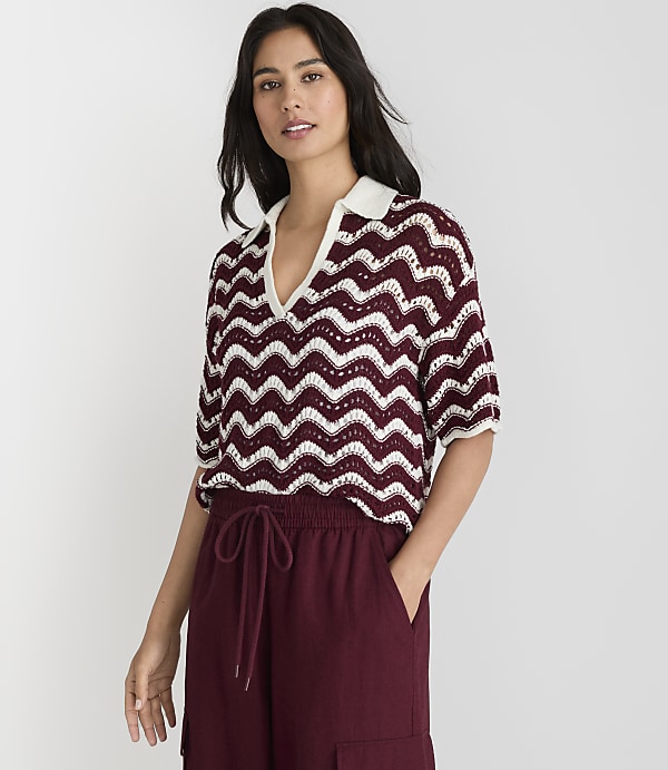 A woman in a burgundy and white chevron-patterned knit polo shirt and burgundy pants stands against a plain white background.