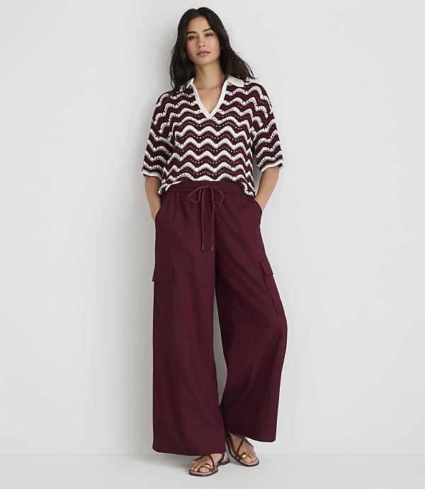 A woman in a chevron-patterned top and maroon wide-leg pants stands against a plain white background.