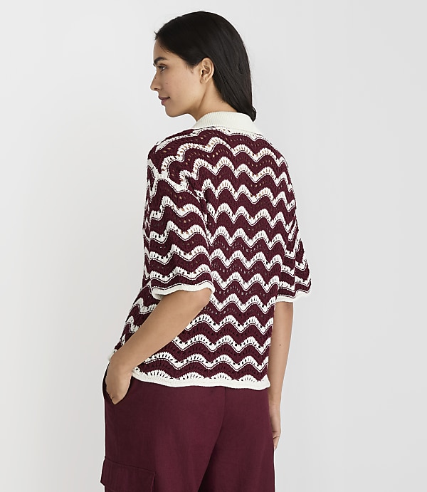 A woman in a burgundy and white chevron knit top and burgundy pants stands with her back to the viewer against a plain white background.