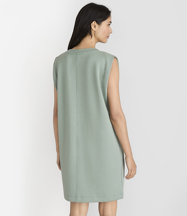 A woman in a light green sleeveless dress stands against a plain white background.