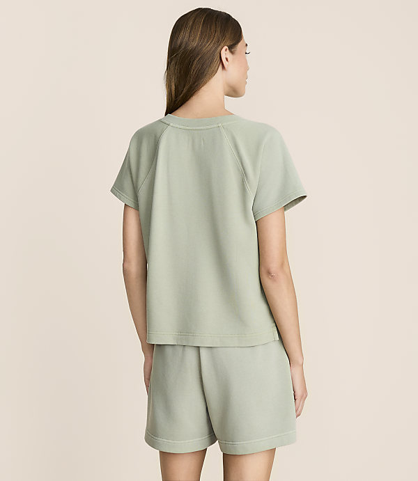 A woman in a light green t-shirt and shorts stands against a plain, light beige background.