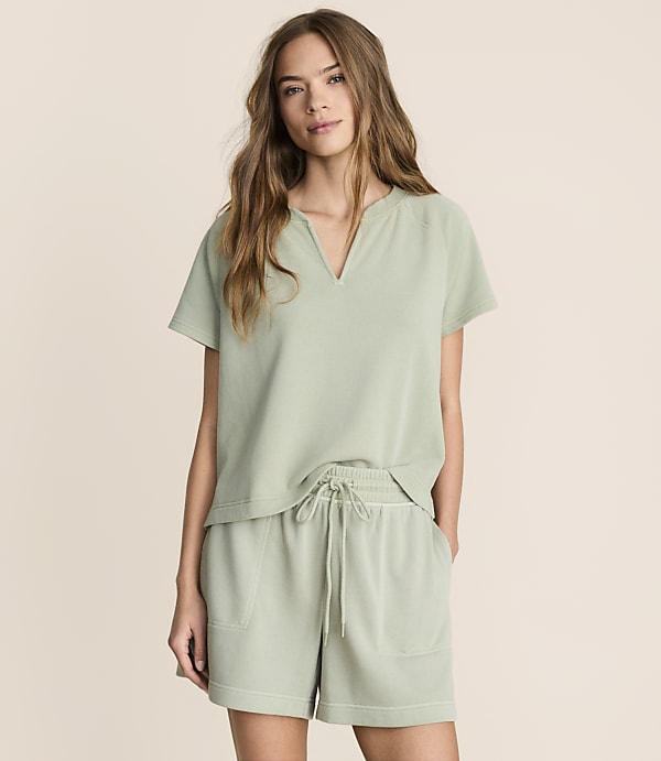 A woman in a light green top and shorts stands against a plain, light-colored background.
