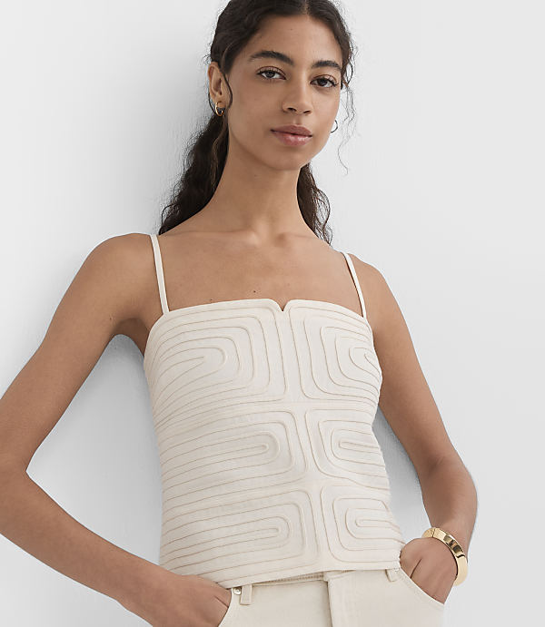 A woman in a cream-colored camisole and pants stands against a plain white background.