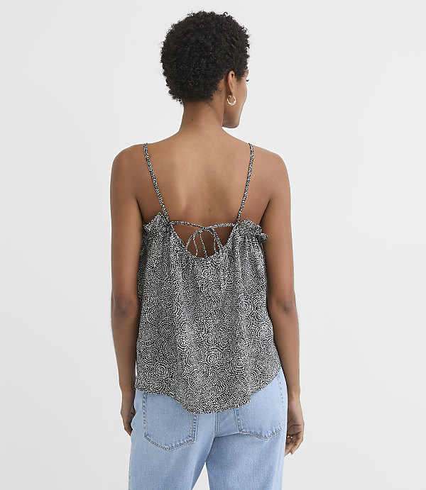 A woman in a patterned camisole and jeans stands against a plain white background.
