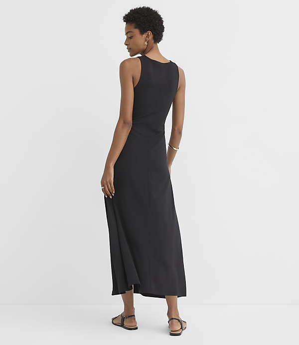 A woman in a black maxi dress stands against a plain white background.