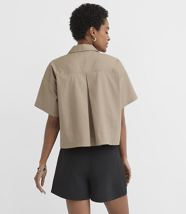 A woman in a tan cropped shirt and black shorts stands against a plain white background.