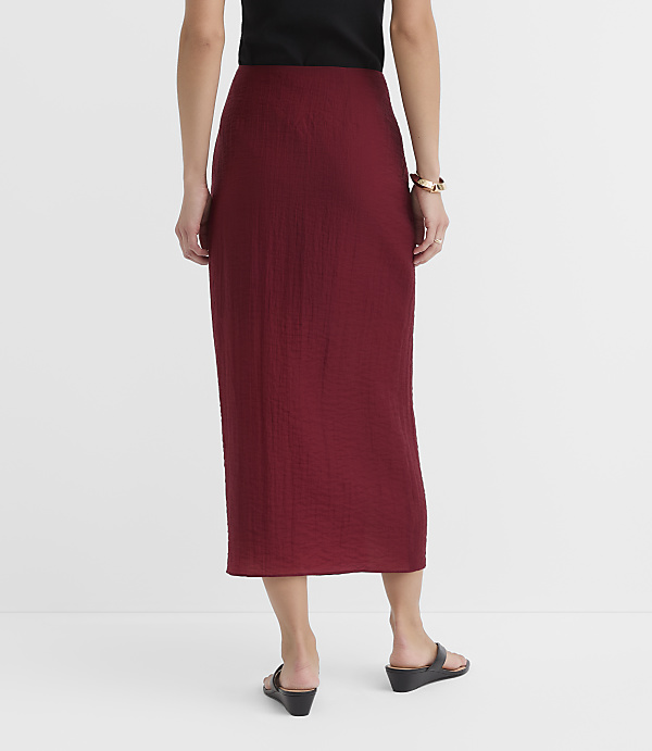A woman in a maroon textured skirt and black top stands against a plain white background.
