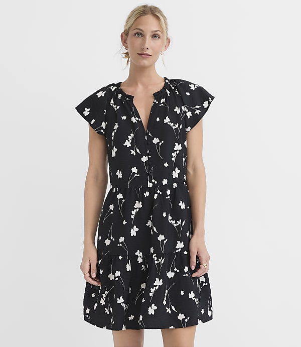 A woman in a black floral dress stands against a plain white background.