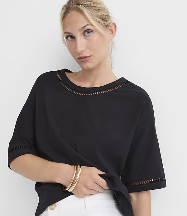 A woman in a black top with cut-out details on the neckline and sleeves poses against a plain white background.