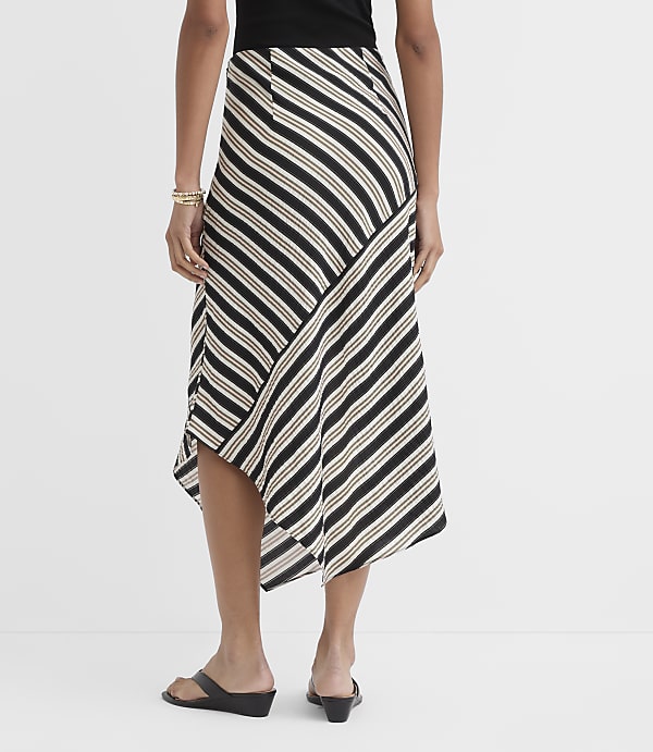 A woman in a striped asymmetrical skirt and black sandals stands against a plain white background.