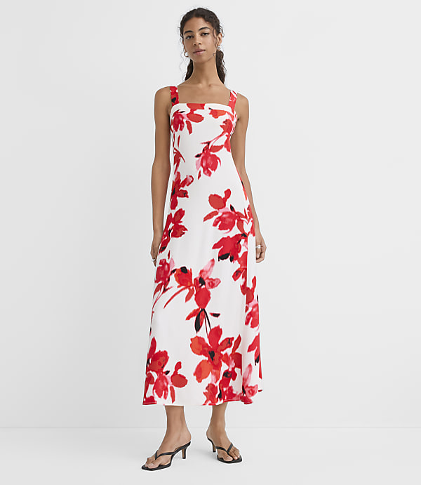 A woman in a white floral dress stands against a plain white background.