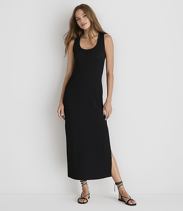 A woman in a black maxi dress stands against a plain white background.