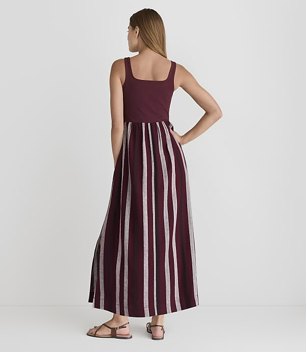 A woman in a maroon and white striped maxi dress stands against a plain white background.
