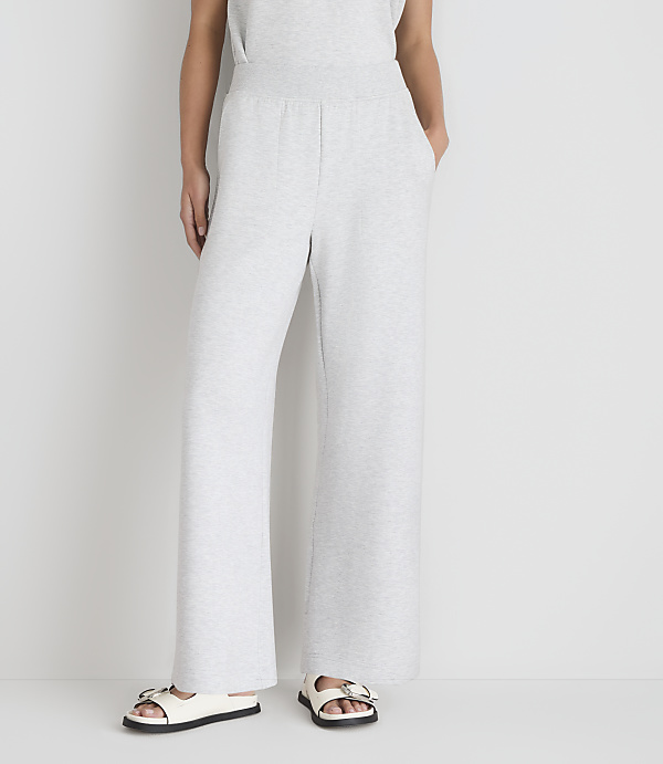 A person wearing light gray wide-leg sweatpants and white sandals stands against a plain white background.