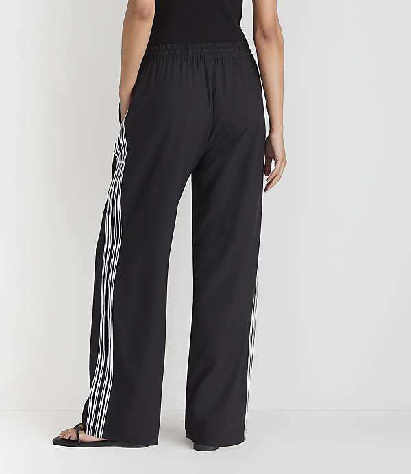 A person wearing black wide-leg pants with white stripes stands against a plain white background.