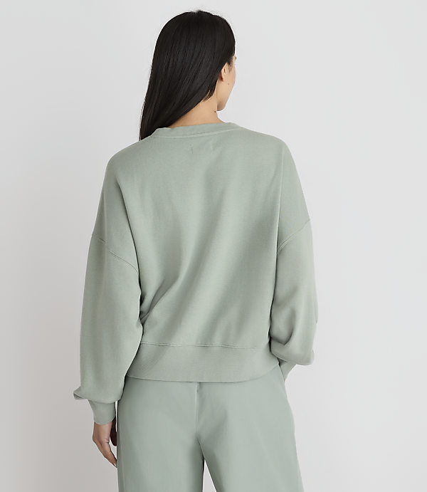 A woman in a light green sweatshirt and pants stands with her back to the camera against a plain white background.