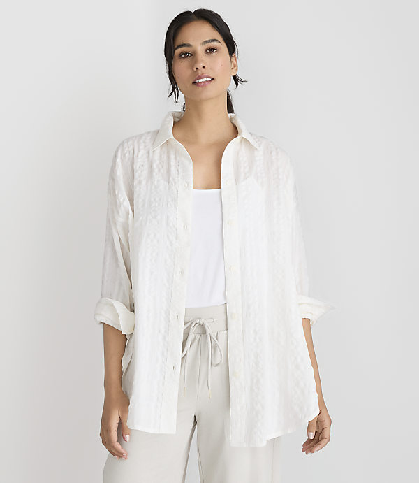 A woman in a white textured shirt and light-colored pants stands against a plain white background.