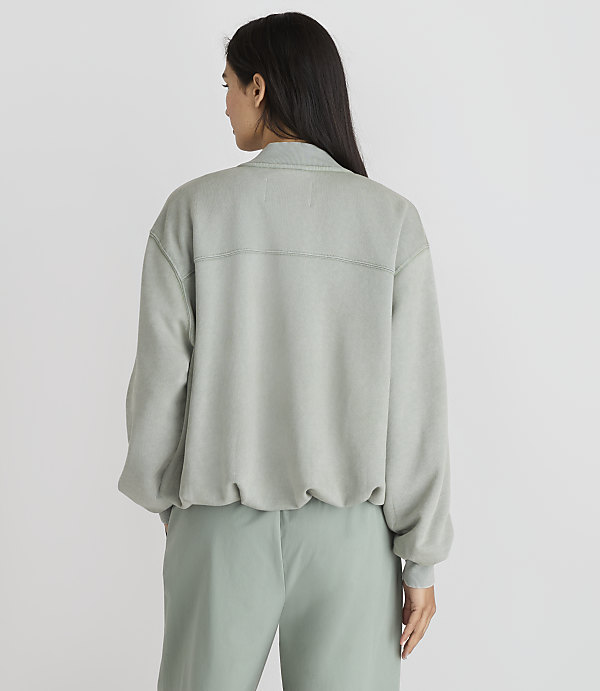 A woman in a light green sweatshirt and pants stands against a plain white background.