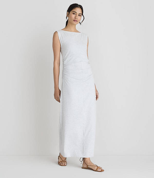 A woman in a light-colored, ruched maxi dress stands against a plain white background.