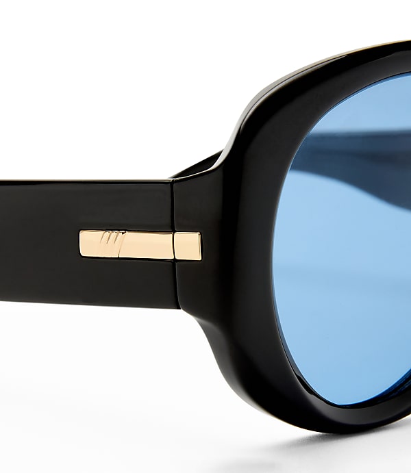A close-up of black sunglasses with gold accents and bright blue lenses is set against a stark white background.