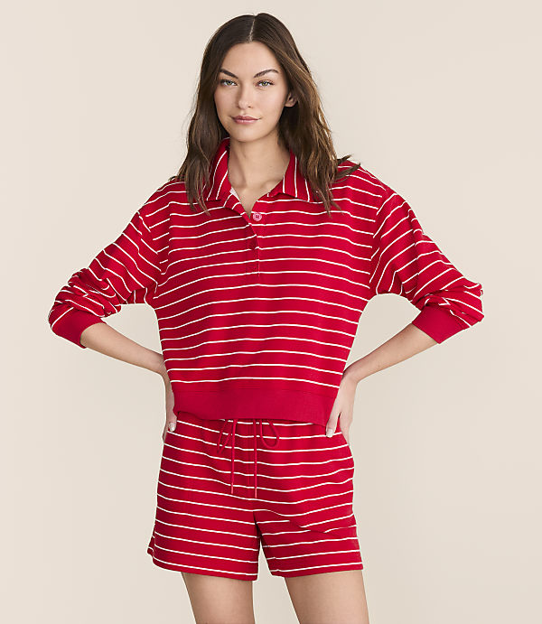 A woman in a red and white striped polo shirt and matching shorts stands against a plain, light-colored background.