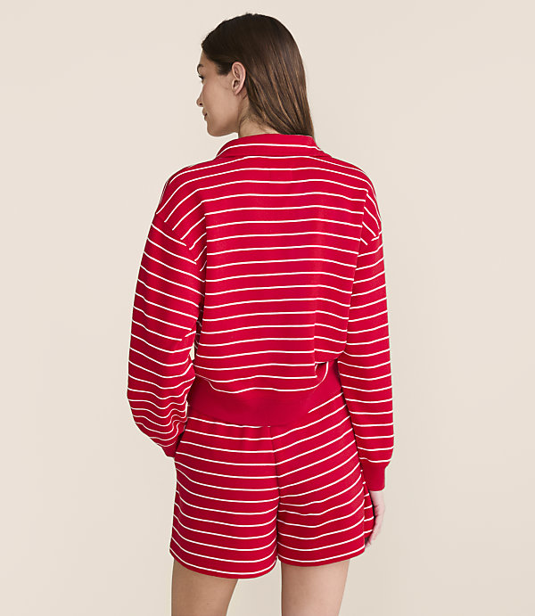 A woman in a red and white striped sweatshirt and shorts stands against a plain, light-colored background.