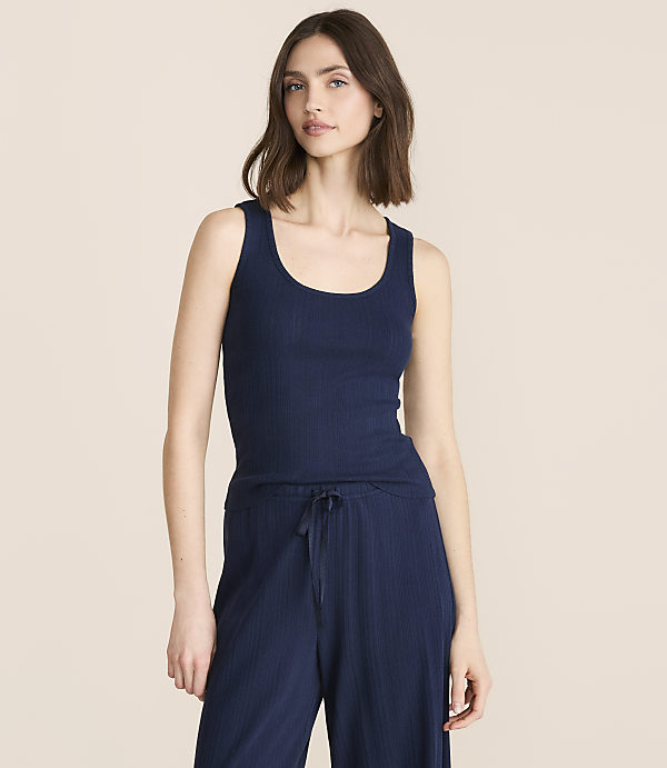 A woman in a light blue ribbed tank top and matching pajama bottoms stands against a plain white background.