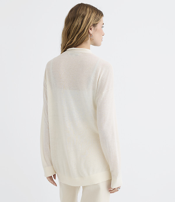 A woman in a cream-colored sweater and pants stands against a plain white background.