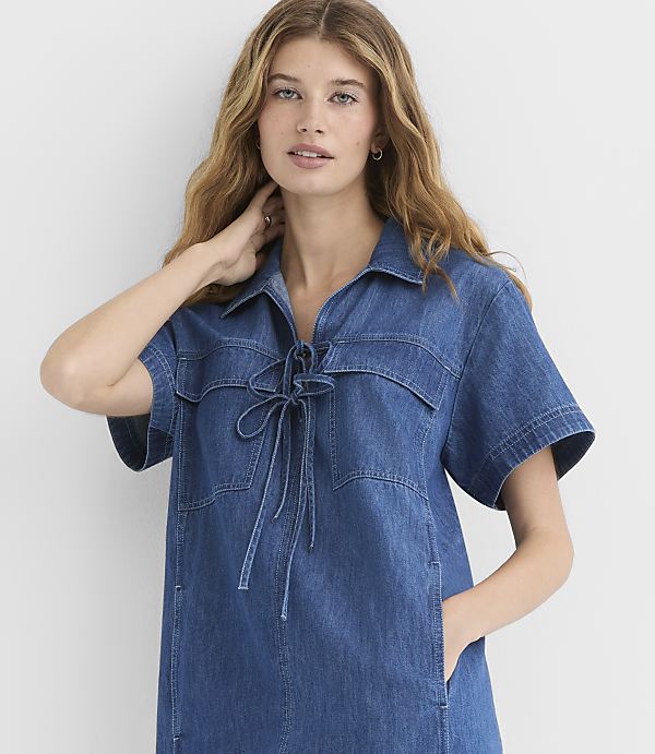 A woman in a denim dress stands against a plain white background.