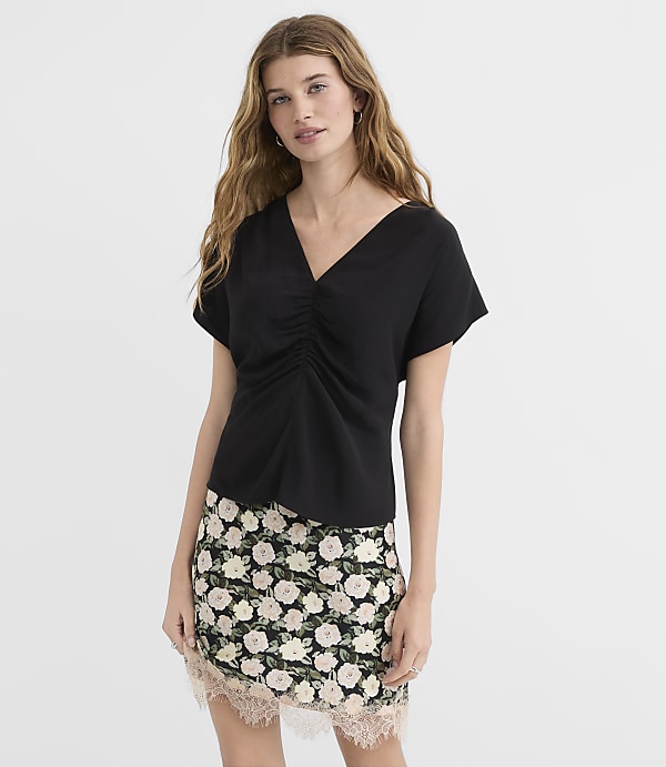 A woman in a black ruched top and floral skirt stands against a plain white background.