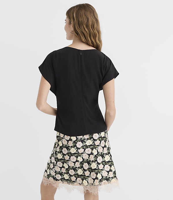 A woman in a black top and floral skirt stands against a plain white background.