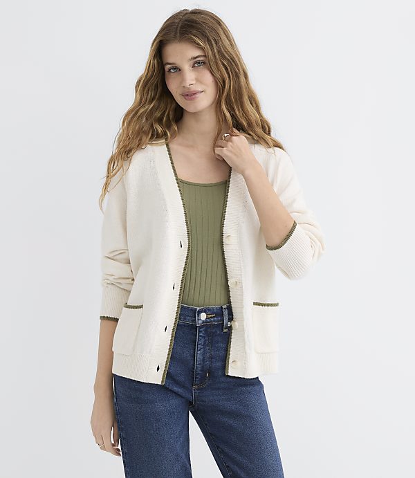 A woman in a cream cardigan and green top stands against a plain white background.