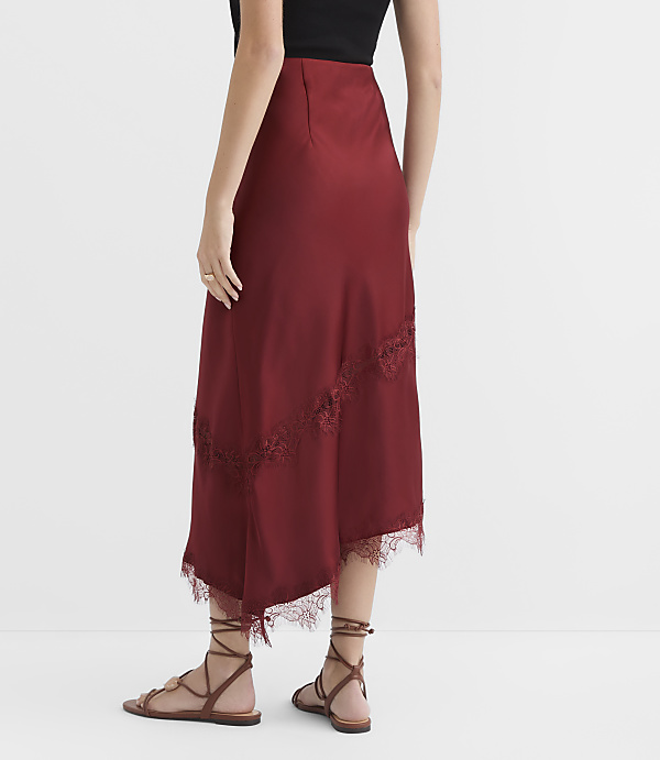 A woman in a burgundy satin skirt with lace trim stands on a white floor, with a plain white background behind her.