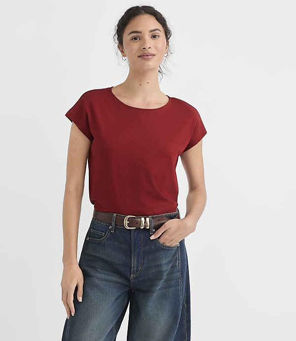 A woman in a red t-shirt and blue jeans stands against a plain white background.