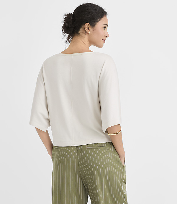 A woman in a light-colored top and green pinstripe pants stands with her back to the viewer against a plain white background.