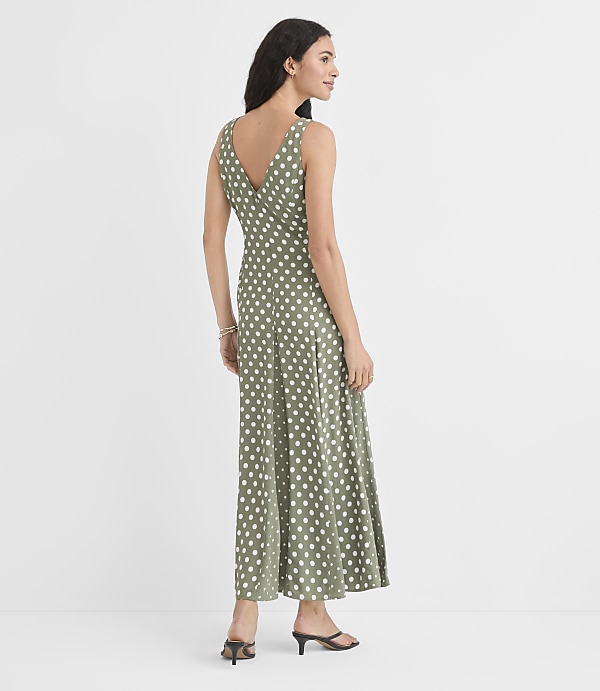 A woman in a green polka dot dress stands against a plain white background.