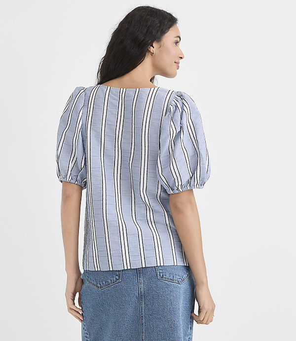 A woman in a blue and white striped puff-sleeve top and denim skirt stands against a plain white background.