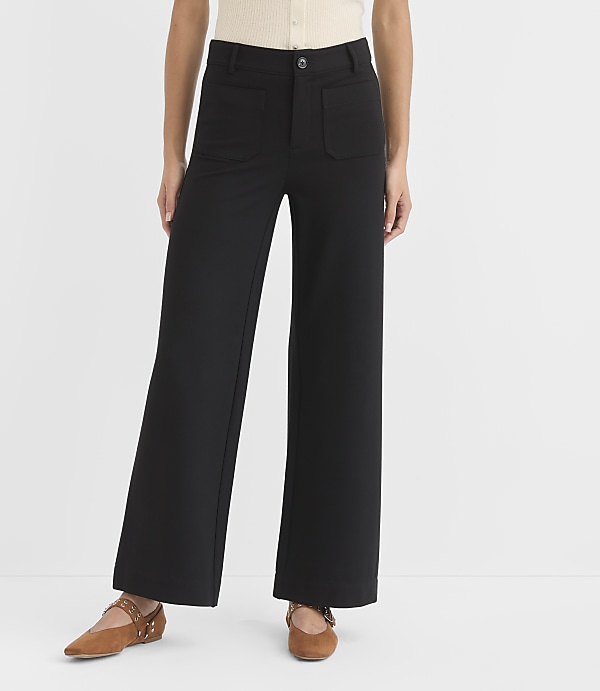 A person stands in black wide-leg pants and brown flats against a plain white background.