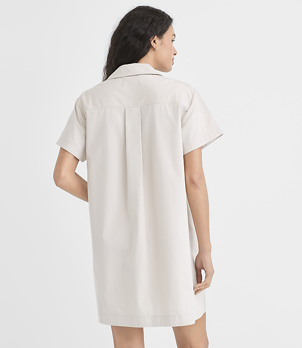 A woman in a light-colored shirt dress stands against a plain white background.