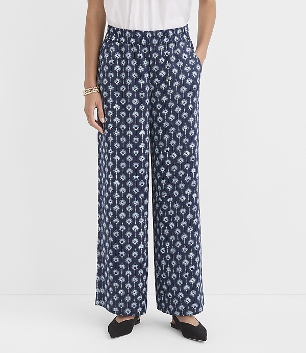 A person stands in the foreground wearing wide-leg patterned pants and black flats, against a plain white background.