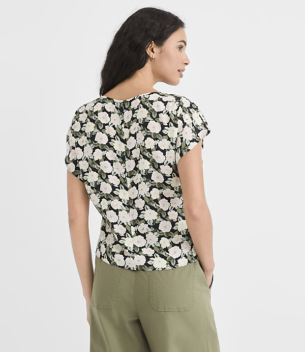 A woman in a floral top and olive green pants stands against a plain white background.