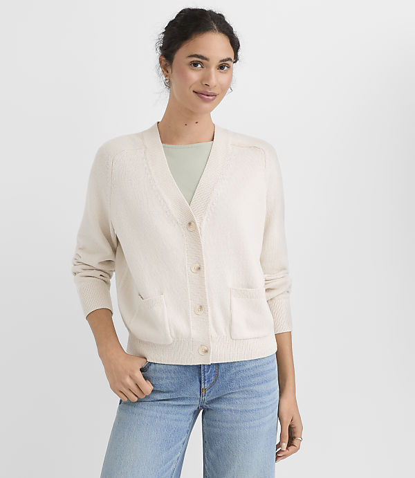 A woman in a cream cardigan and blue jeans stands against a plain white background.