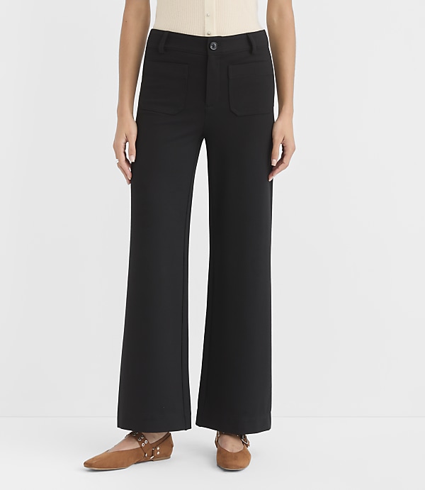 A person stands in black wide-leg pants and brown flats against a plain white background.