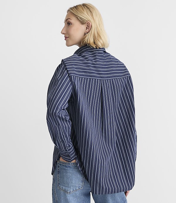 A woman in a blue and white striped shirt and jeans stands against a plain white background.