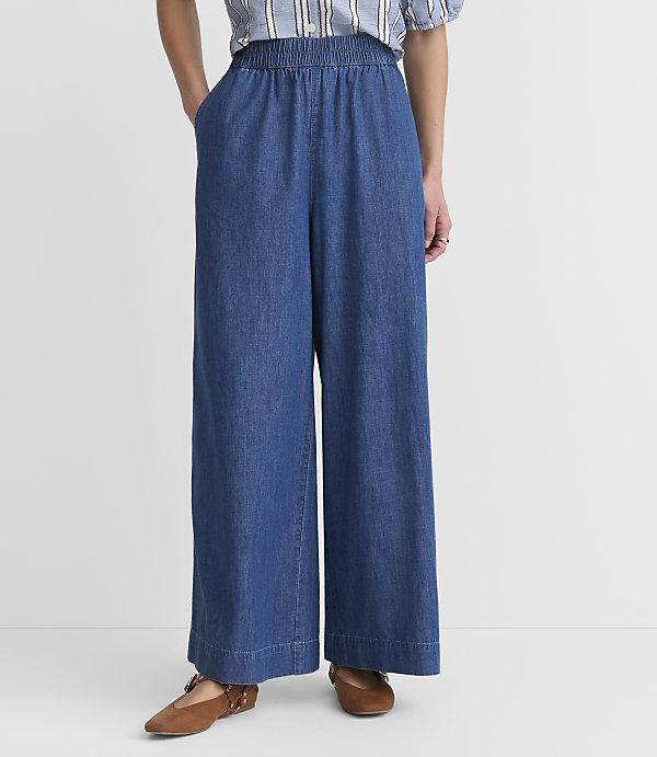 A person stands in wide-leg denim pants and brown flats against a plain white background.
