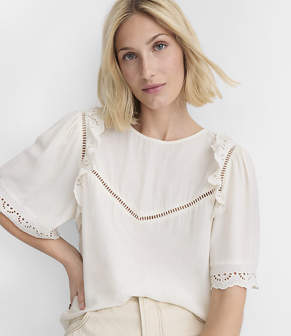 A blonde woman in a white ruffled blouse poses against a plain white background.