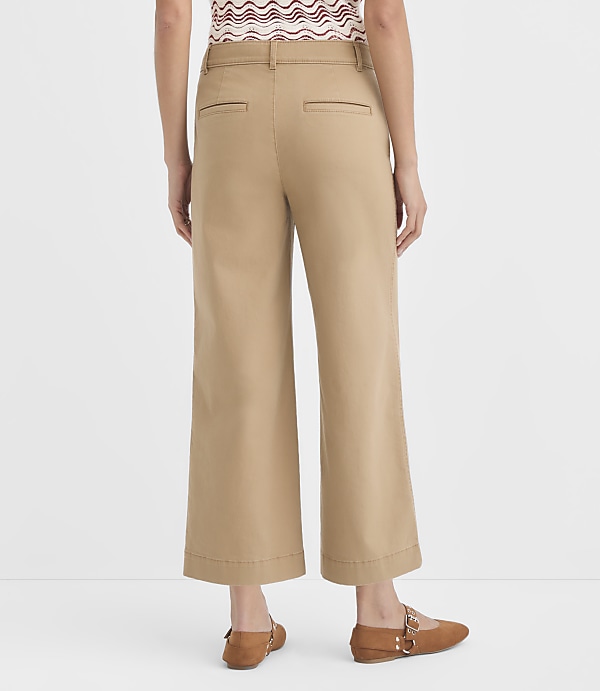 A person wearing tan cropped wide-leg pants and brown flats stands against a plain white background.