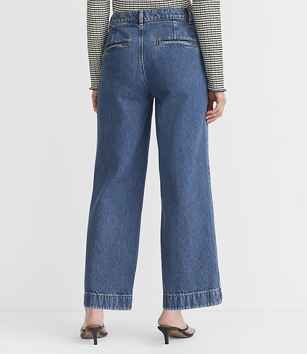 A person wearing wide-leg denim jeans and a striped shirt stands against a plain white background.